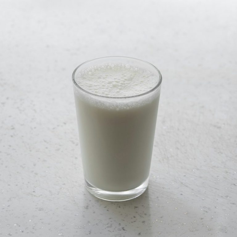 Ein Glas Milch auf einer hellen, glatten Oberfläche.